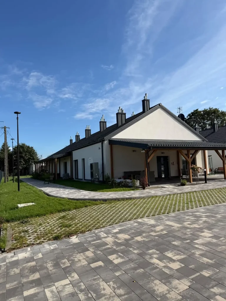 Parterowy budynek mieszkań wspomaganych w Kraszewie Gaczułty z zadaszonym wejściem i chodnikiem